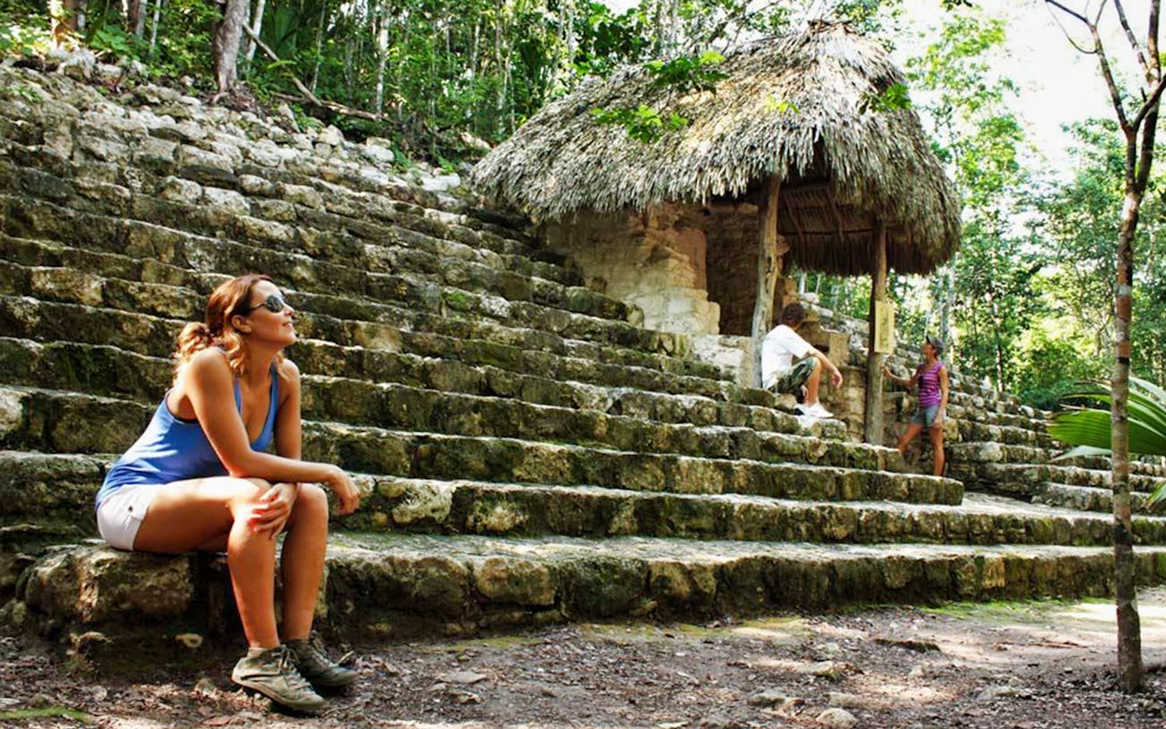 Visitors resting on ancient stone steps in Coba, surrounded by lush jungle.