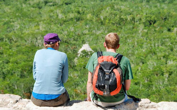 Two people sitting on a ledge overlooking the jungle at Coba, Mexico.