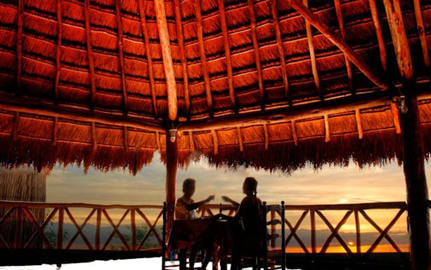 Two people dining under a thatched roof at sunset in Coba, Mexico.