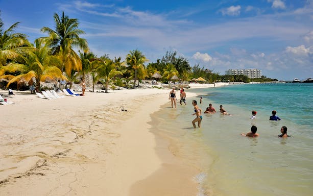 Beachgoers enjoying the water and sandy shore on Isla Mujeres during a sailing tour.