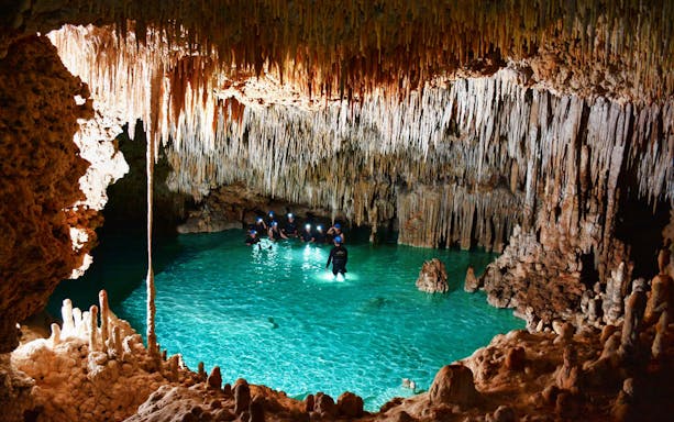 Visitors exploring the underground river at Rio Secreto Reserve, surrounded by stalactites.