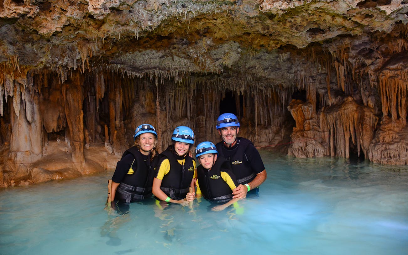Family exploring Rio Secreto's underground river with stalactites in the background.