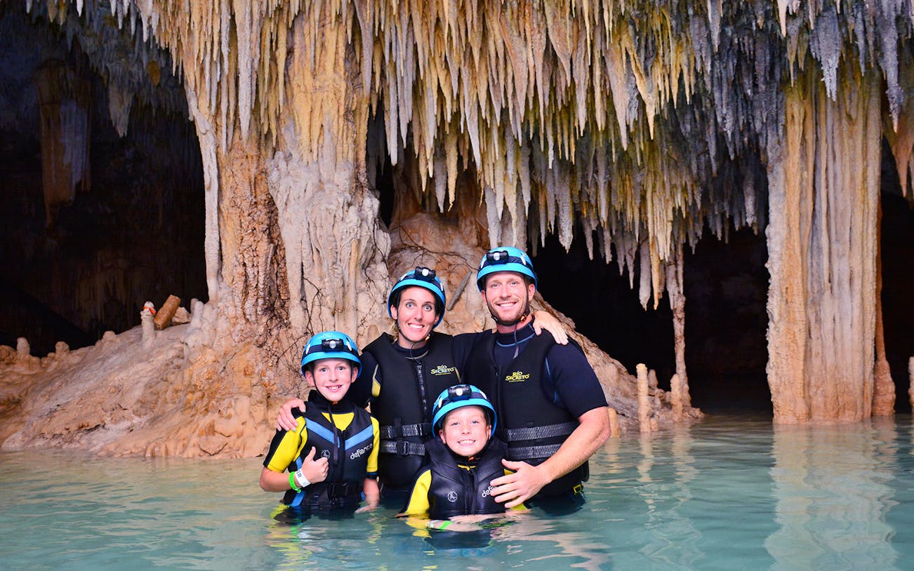 Family exploring Rio Secreto's underground river with stalactites in the background.