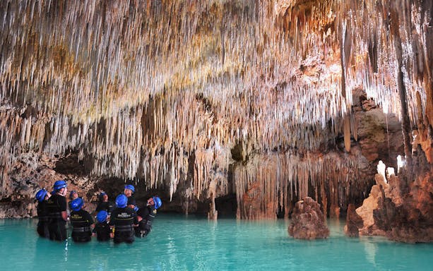 Visitors exploring stalactites in Rio Secreto's underground river, Mexico.