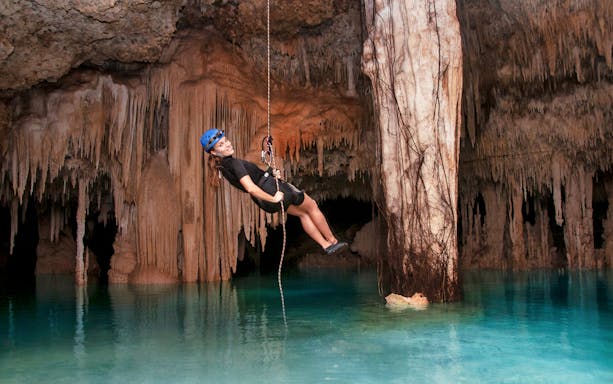 Person rappelling in Rio Secreto cave with stalactites and turquoise water.