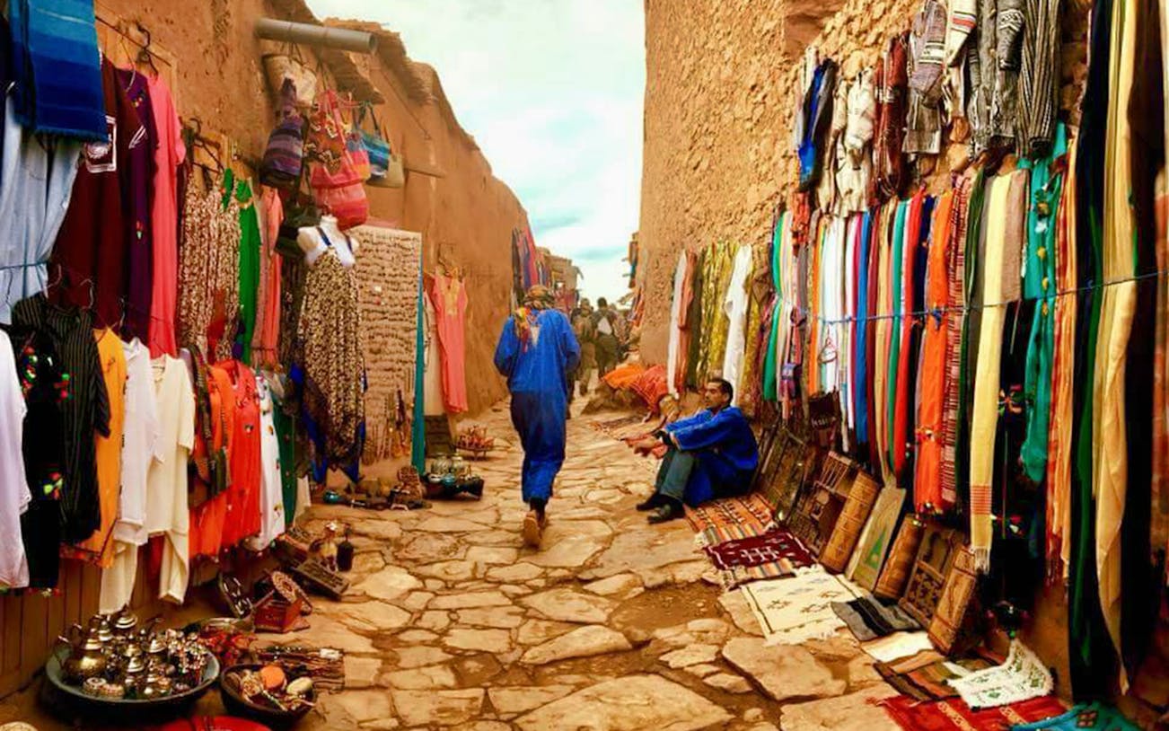 Market street in Ouarzazate with colorful textiles and local crafts on display.