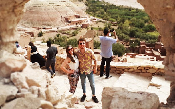 Tourists exploring Kasbah Aït Benhaddou with views of the Atlas Mountains in Ouarzazate.