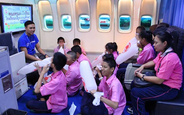 Children in a flight simulation class with instructor, practicing safety procedures.