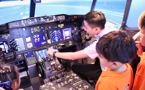 Pilot guiding children in a flight simulator cockpit during Flight Simulation Experience.