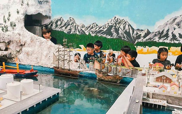 Children observing model ships and landscapes at a miniature exhibit.