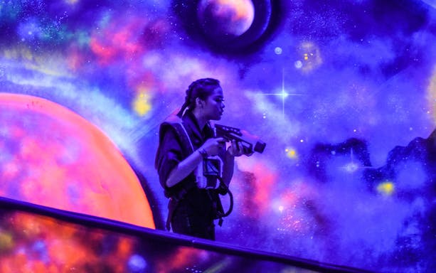 Person playing laser tag at Playsquare Laser Tag, Central World, with a cosmic-themed backdrop.