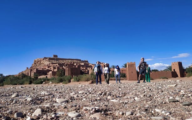Tourists exploring Kasbah Aït Benhaddou with Atlas Mountains backdrop in Ouarzazate.