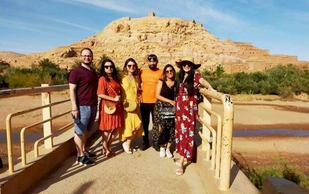 Group of tourists at Kasbah Aït Benhaddou, Ouarzazate, with desert landscape in background.