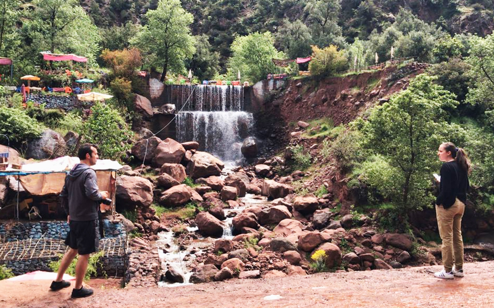 Visitors exploring a waterfall in Ourika Valley, surrounded by lush greenery and rocky terrain in the High Atlas Mountains.