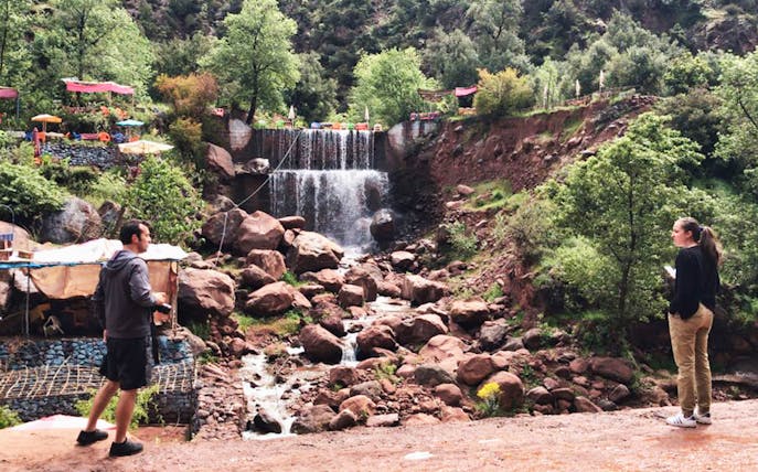 Visitors exploring a waterfall in Ourika Valley, surrounded by lush greenery and rocky terrain in the High Atlas Mountains.