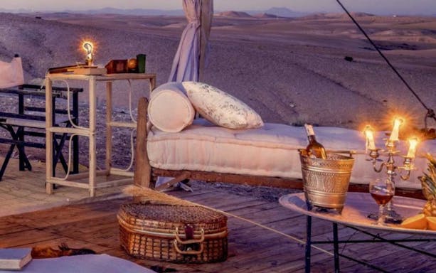 Outdoor lounge setup in Agafay Desert with table, wine, and candles for a private dinner under the stars.