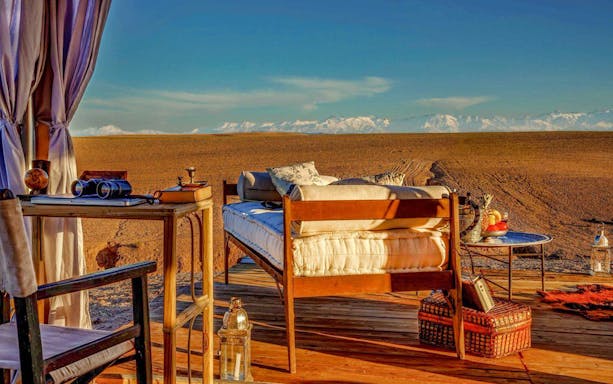 Outdoor setup in Agafay Desert with bed, table, and distant mountains for a private tour experience.
