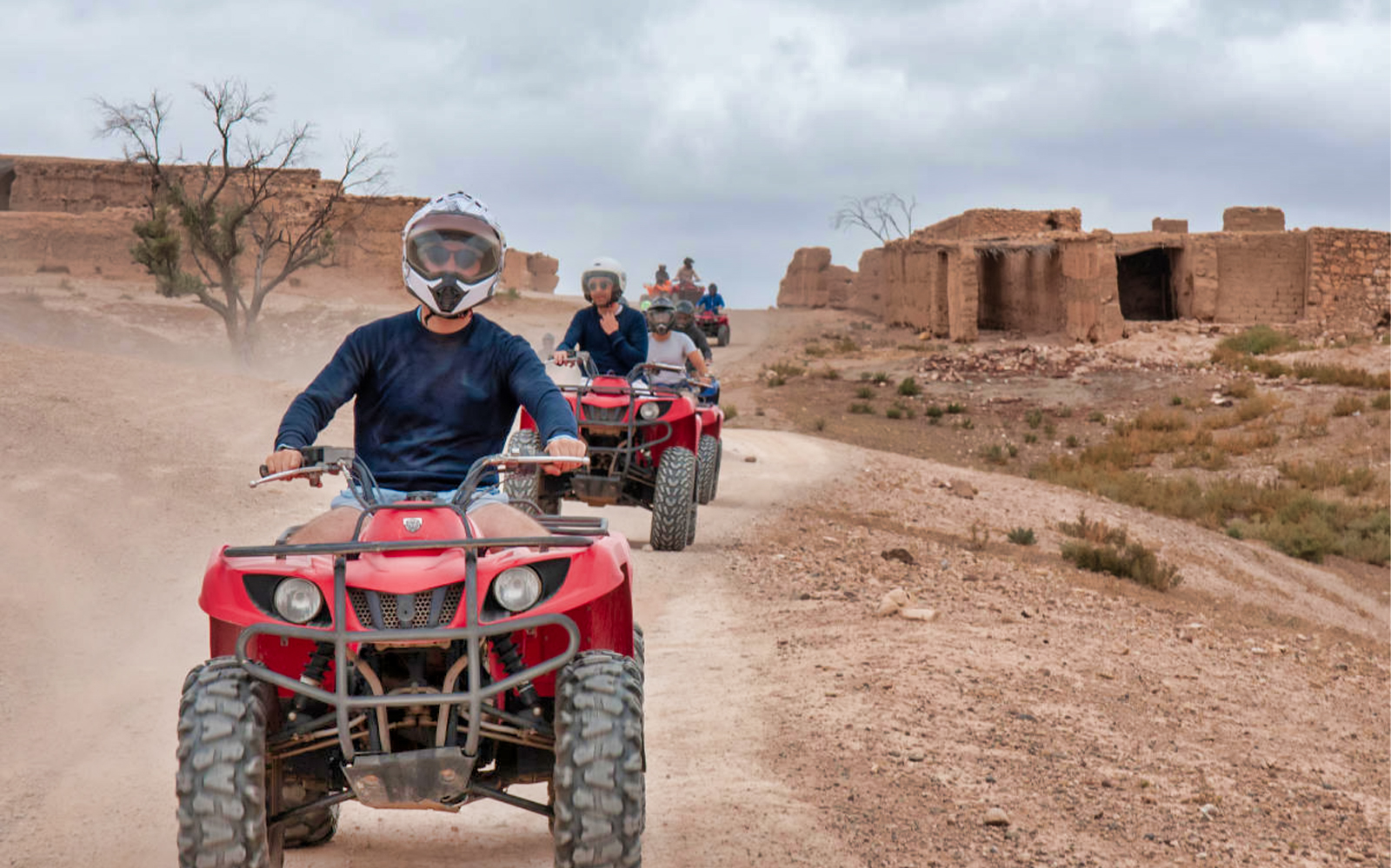 Quad biking tour through Agafay Desert near Marrakech with ancient ruins in the background.