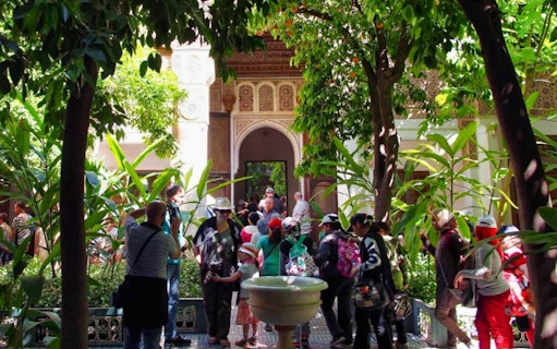 Tourists exploring a lush courtyard in Marrakesh during a palaces and monuments guided tour.