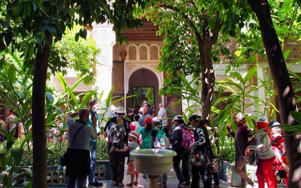 Tourists exploring a lush courtyard in Marrakesh during a palaces and monuments guided tour.