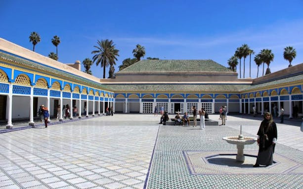 Bahia Palace courtyard with tourists in Marrakesh, featuring colorful arches and palm trees.