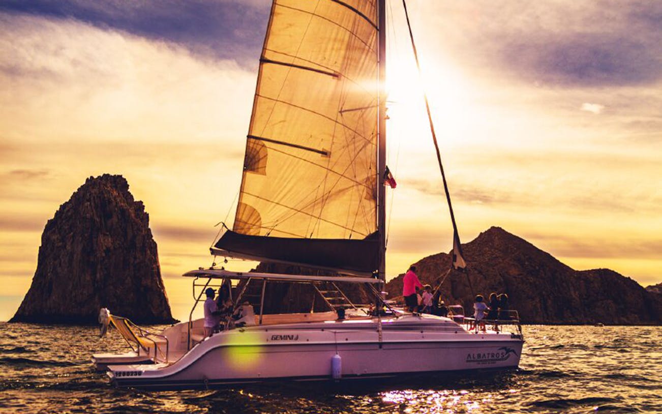 Sailboat cruising near rock formations at sunset in Cabo San Lucas.