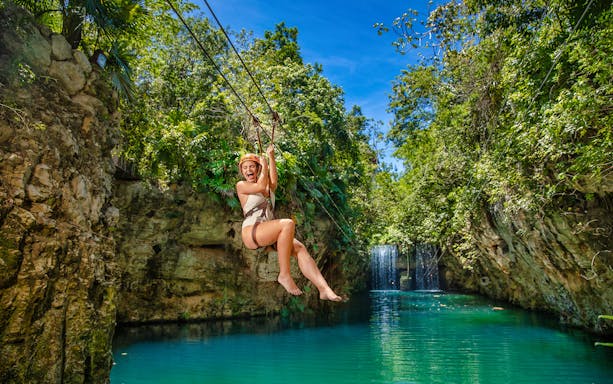Ziplining over a turquoise river at Xplor Park with lush greenery and waterfall.