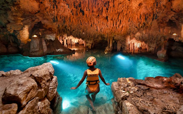 Person exploring a cave with stalactites and clear water at Xplor Park.