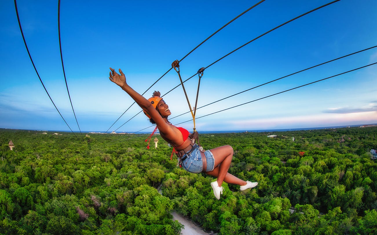 Person ziplining over lush forest at Xplor Park, Mexico.
