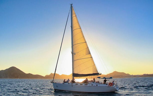 Sailboat at sunset near Cabo San Lucas with passengers enjoying the view.