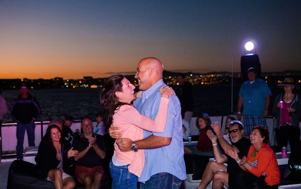 Couple dancing on a sunset cruise in Cabo San Lucas with people clapping.