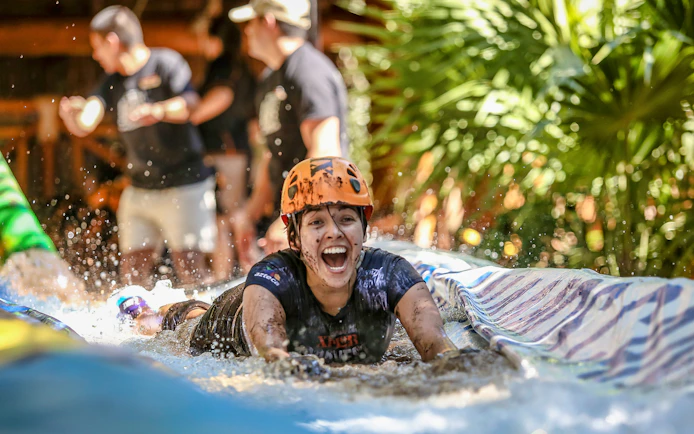 Person enjoying a water slide at Xplor Park, wearing a helmet and surrounded by greenery.