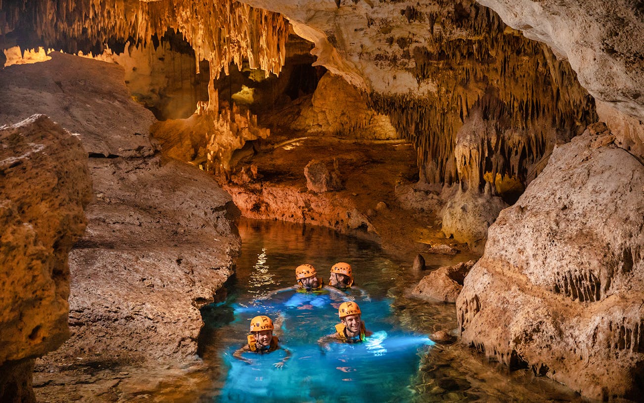 Visitors exploring an underground river at Xplor Fuego Park, surrounded by stalactites.