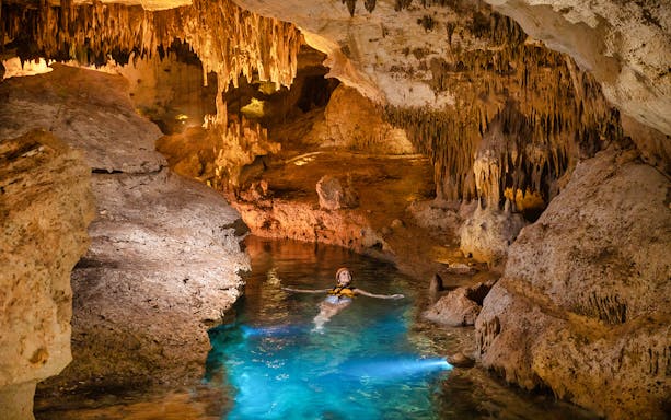 Person swimming in an illuminated underground cave at Xplor Fuego Park.