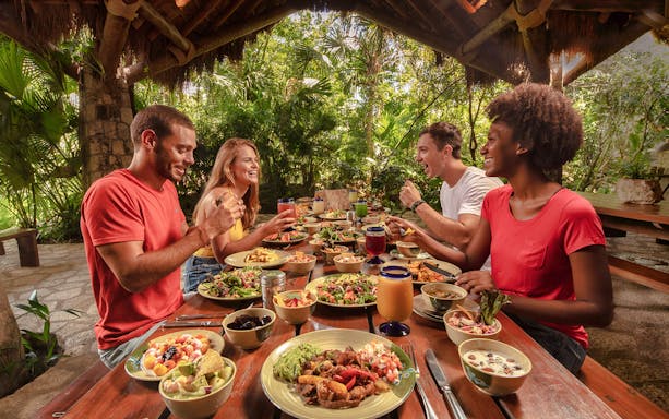 Visitors enjoying a meal at Xplor Fuego Park with diverse dishes on a wooden table.