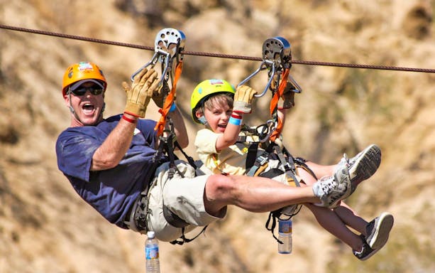Adults and child ziplining in Los Cabos canyon, wearing helmets and harnesses.