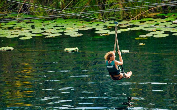 Ziplining over water at Xenotes Park during 1-day tour with lunch and transportation.