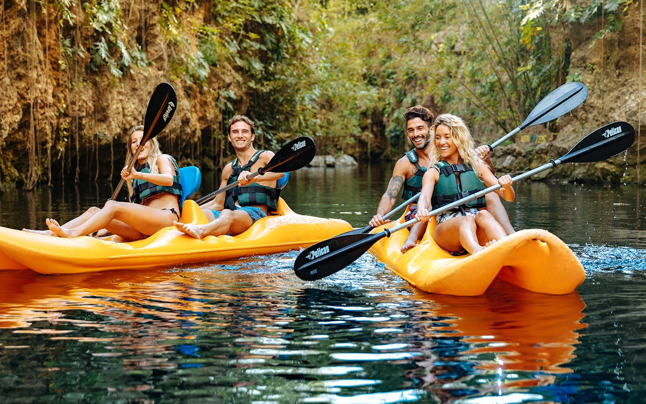 Kayaking in Xenotes Park, Mexico, with lush greenery and rocky cliffs in the background.