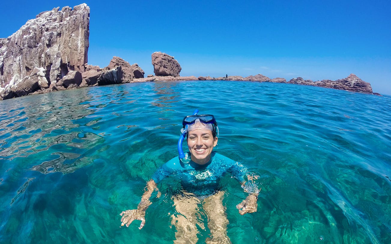 Snorkeler enjoying clear waters near rocky cliffs in Cabo San Lucas, Sea of Cortez.