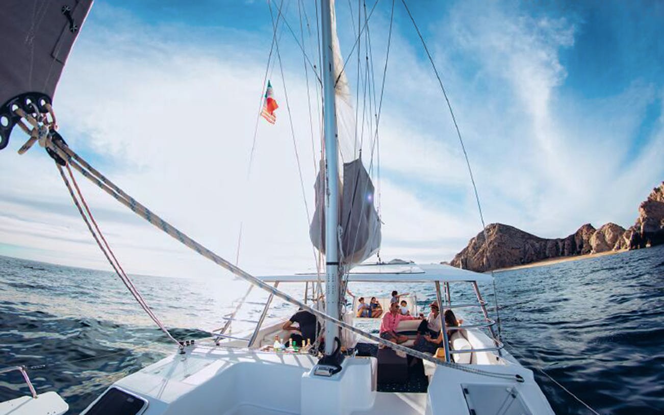 Sailing tour in Cabo San Lucas with passengers enjoying views of the ocean and rocky coastline.