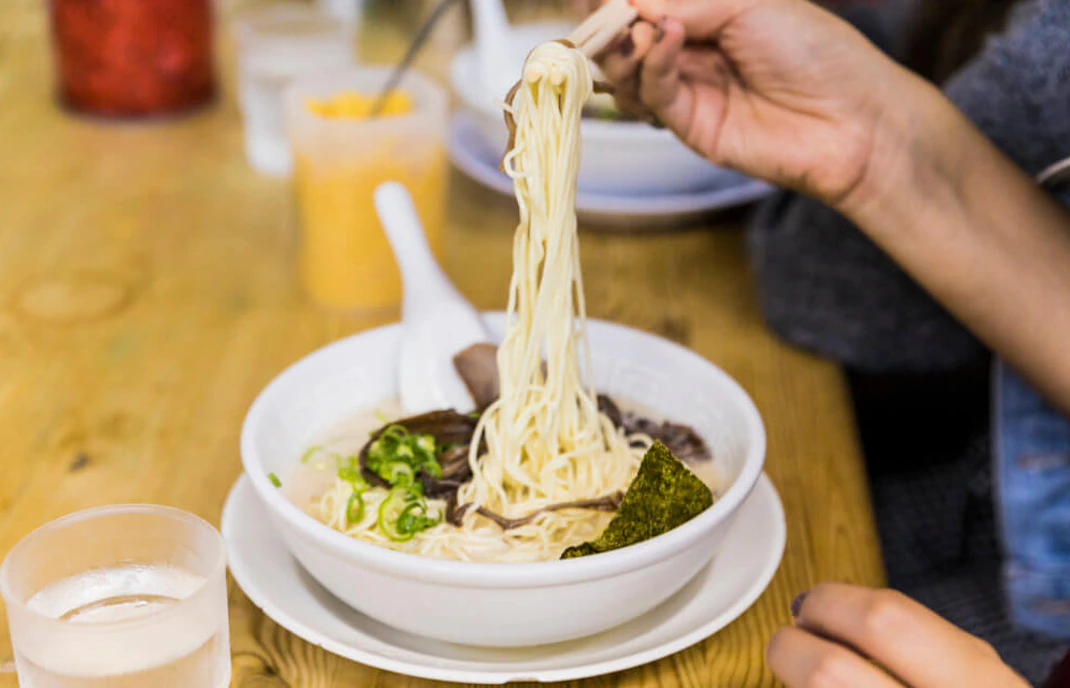 Chopsticks lifting ramen noodles in a bowl, Shibuya virtual tour experience.