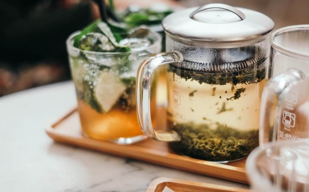 Teapot with green tea and a cocktail with lime and mint on a wooden tray, Japan.