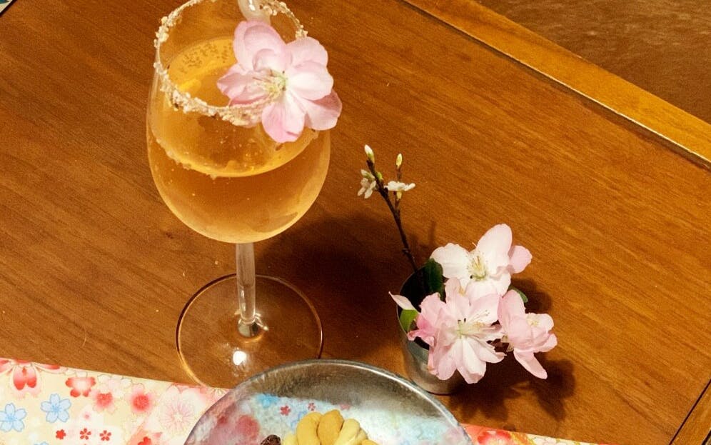 Cocktail with cherry blossom garnish on a table during online happy hour in Japan.