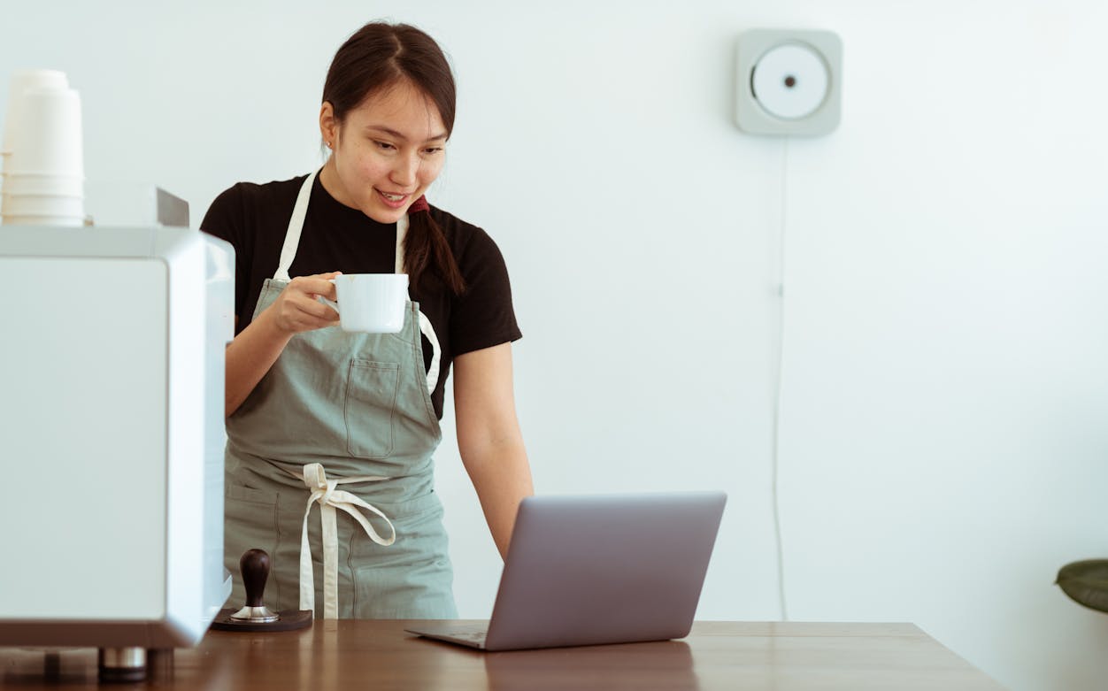 Person in apron holding a cup, engaging in an online cooking class.