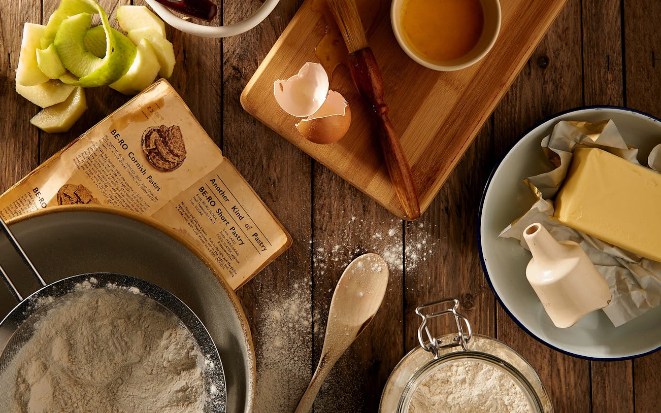 Baking ingredients and recipe book on a wooden table for an interactive cooking experience.