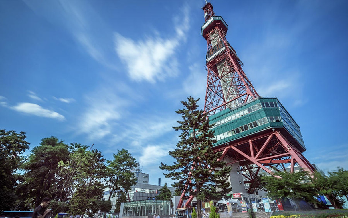 Sapporo TV Tower with surrounding trees and clear blue sky.