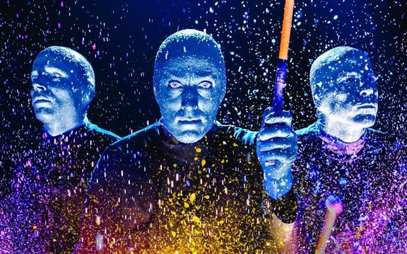 Blue Man Group performers with paint splashes during a live show.