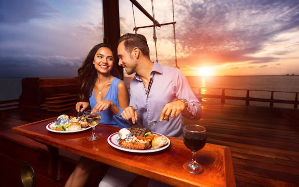 Couple dining on a boat at sunset in Tulum, enjoying a meal with wine.