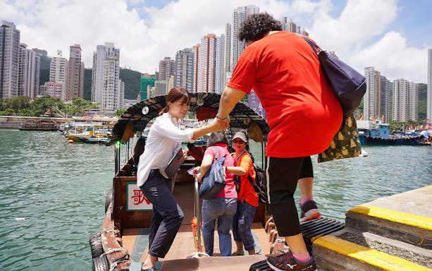 Tourists boarding a boat in Aberdeen, Hong Kong, with high-rise buildings in the background.