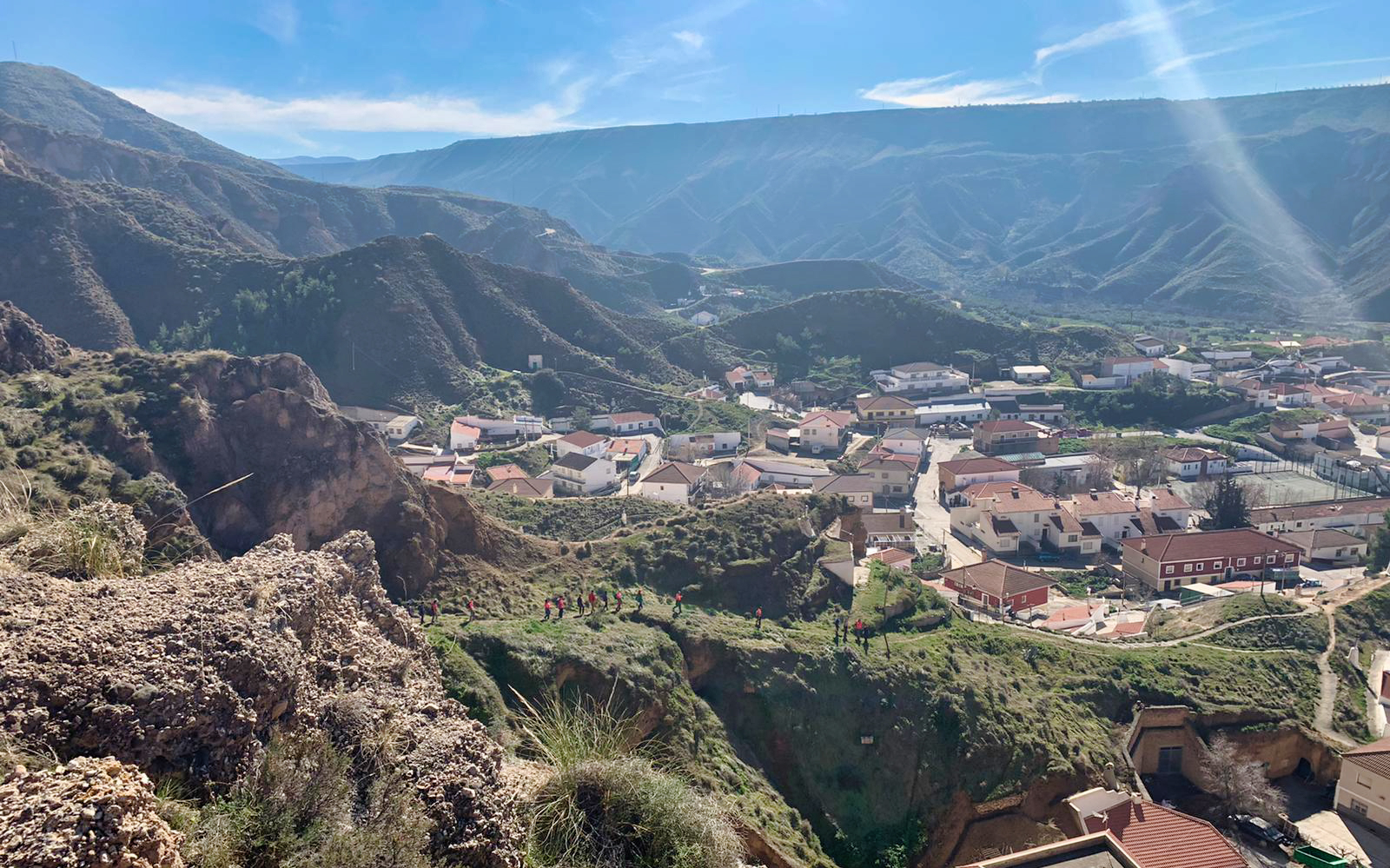 Granada Geopark village view with hikers on a trail, surrounded by rugged hills.
